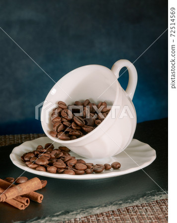 Coffee roasted beans with cinnamon sticks in white ceramic mug blue background 72514569
