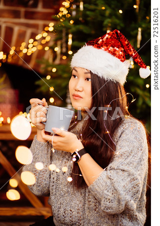 A beautiful woman sits on floor near fireplace in house decorated for new year. A beautiful woman sits on floor near fireplace in house decorated for new year. 72516201