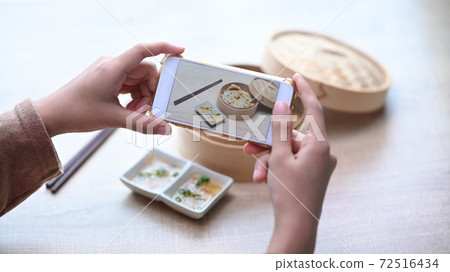 Woman using smart phone taking photo of original Japanese dumplings on wooden table. 72516434
