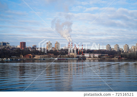 from boiler room tube goes white steam, smoke into sky. Cityscape by river 72516521