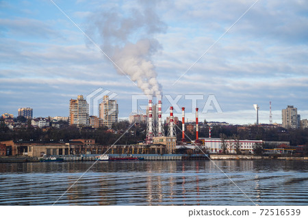from boiler room tube goes white steam, smoke into sky. Cityscape by river from boiler room tube goes white steam, smoke into sky. Cityscape by river 72516539