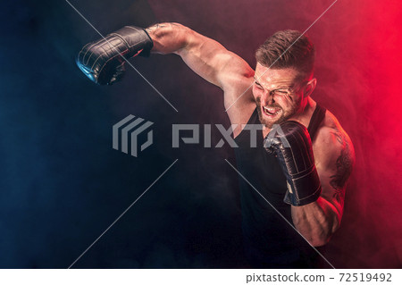 Bearded tattooed sportsman muay thai boxer in black undershirt and boxing gloves fighting on dark background with smoke. Bearded tattooed sportsman muay thai boxer in black undershirt and boxing gloves fighting on dark background with smoke. 72519492