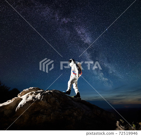 Spaceman walking up the rocky hill under beautiful starry sky. Spaceman walking up the rocky hill under beautiful starry sky. 72519946
