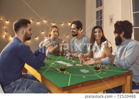 Group of excited friends with playing cards in hands sitting, betting and playing poker Group of excited friends with playing cards in hands sitting, betting and playing poker 72520488