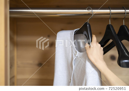 A woman's hand hanging clothes in a wood-grained closet A woman's hand hanging clothes in a wood-grained closet 72520951