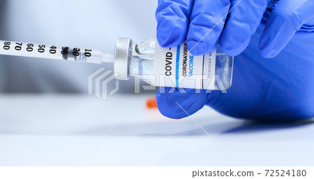 Close-up of infectious doctor or nurse in latex blue rubber gloves holds a syringe and Covid-19 coronavirus vaccine vial 72524180