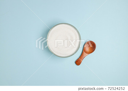 Top view of collagen powder or powder in a glass bowl and small wooden spoon on a blue background with a copy space 72524252