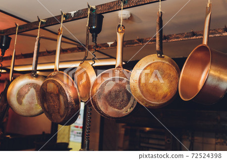 Old kitchen pans hanging on the bar. Different size of pans on the wall, Home decoration, Kitchen background. Old kitchen pans hanging on the bar. Different size of pans on the wall, Home decoration, Kitchen background. 72524398