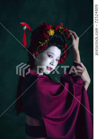 Young japanese woman as geisha on dark green background. Retro style, comparison of eras concept. Young japanese woman as geisha on dark green background. Retro style, comparison of eras concept. 72524909