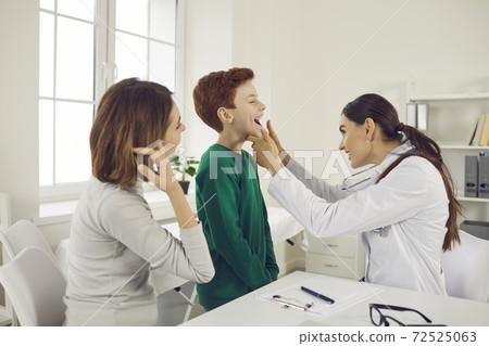 Pediatrician woman checks for sore throat of a boy who came for an examination with his mother. 72525063