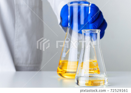 Scientist or doctor in blue gloves pouring some yellow liquid into a flask 72529161