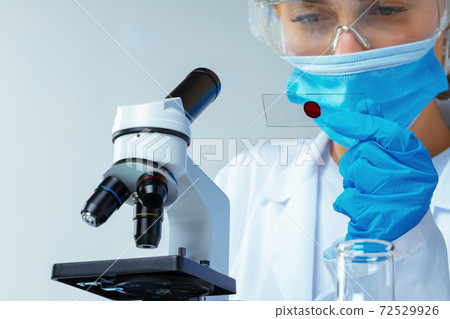 Woman scientist looking at slide with blood sample near microscope in laboratory 72529926