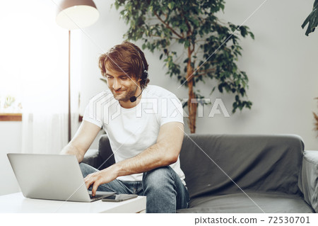 Young man businessman with headset working on laptop from home 72530701