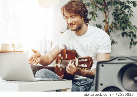 Young man watching guitar tutorial on his laptop Young man watching guitar tutorial on his laptop 72530826