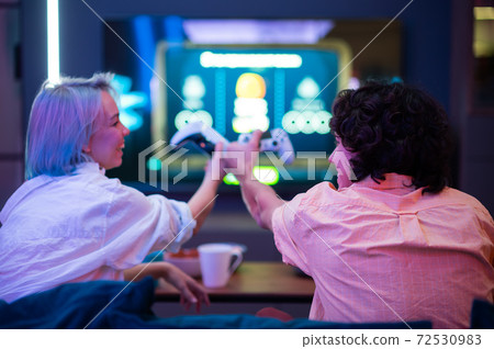 Happy couple playing video games at home during self isolation on a pandemic quarantine. Young man and woman love to spend time together. Back view. 72530983