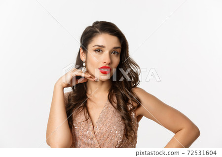 Concept of New Year celebration and winter holidays. Close-up of beautiful elegant woman with red lips and party dress, touching her face and looking at camera, white background 72531604