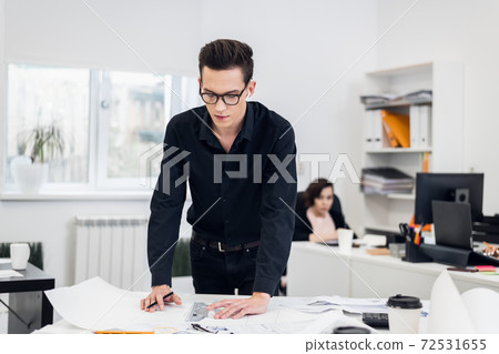 A portrait of a young man in eyeglasses working on some sketches 72531655