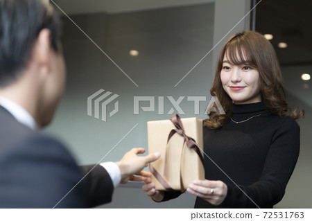 Female subordinate in her 20s handing Valentine's chocolate to her boss Female subordinate in her 20s handing Valentine's chocolate to her boss 72531763