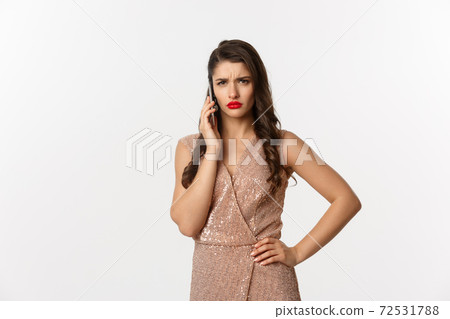 Christmas party and celebration concept. Elegant woman in glamour dress talking on phone and looking displeased, receive bad news, white background 72531788
