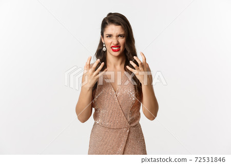 Celebration and party concept. Angry young woman with red lips, wearing luxurious dress, cursing someone and clench fists, grimacing aggressive, standing mad over white background 72531846