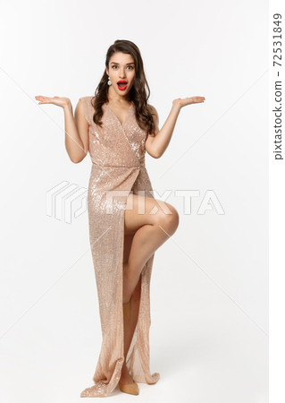 Christmas party and celebration concept. Attractive brunette model in elegant dress, showing two offers, raising hands and holding something on copy space, white background Christmas party and celebration concept. Attractive brunette model in elegant dress, showing two offers, raising hands and holding something on copy space, white background 72531849