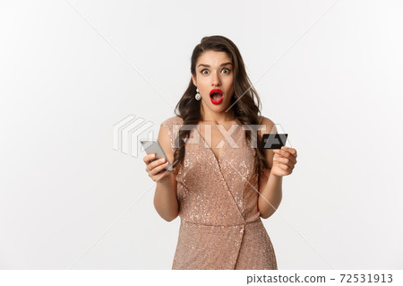 Online shopping and holidays concept. Surprised woman in glamour dress, buying in internet with credit card and mobile phone, looking amazed, white background 72531913
