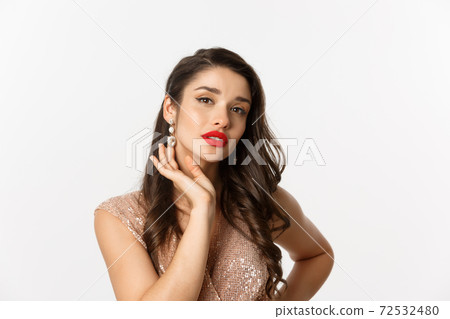 Concept of New Year celebration and winter holidays. Close up of beautiful woman dressed for party, showing luxury earrings and looking sensual at camera, white background Concept of New Year celebration and winter holidays. Close up of beautiful woman dressed for party, showing luxury earrings and looking sensual at camera, white background 72532480
