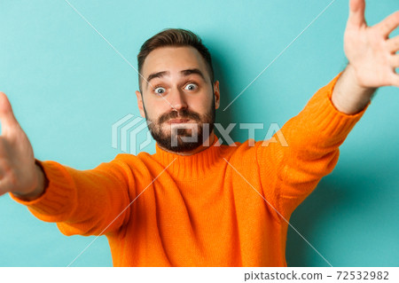 Close-up of handsome happy man reaching hands forward, stretching arms for hug, standing against turquoise background Close-up of handsome happy man reaching hands forward, stretching arms for hug, standing against turquoise background 72532982