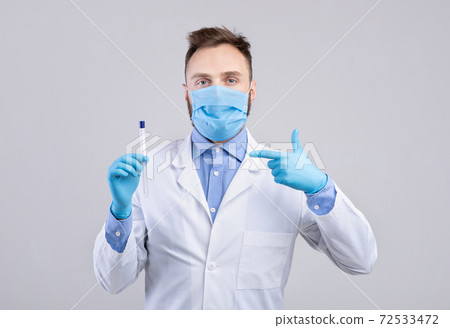 Male doctor wearing protective mask and gloves, pointing at coronavirus PCR test tube on grey studio background 72533472
