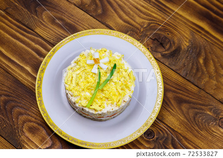 Traditional russian layered salad Mimosa with spring decoration Daffodil. Decoration is made of egg, green onion and carrot. Top view Traditional russian layered salad Mimosa with spring decoration Daffodil. Decoration is made of egg, green onion and carrot. Top view 72533827