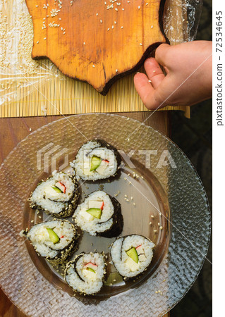 The woman cooked sushi and placed them on a round plate 72534645