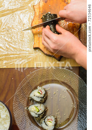 A woman in the kitchen cuts the knife with a roll of sushi at the level of the pieces for visitors A woman in the kitchen cuts the knife with a roll of sushi at the level of the pieces for visitors 72534646