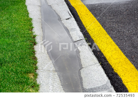 the current rainwater in the filled canal is a cement ditch of the drainage system on the side of a wet asphalt road after rain. the current rainwater in the filled canal is a cement ditch of the drainage system on the side of a wet asphalt road after rain. 72535493