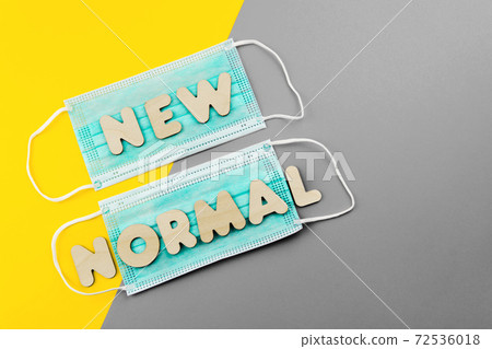 NEW NORMAL words of wooden letters on protective face masks. Post covid-19 pandemic changes, wearing face mask in public concept. Yellow and grey colors. 72536018