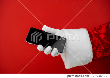 Santa Claus hand holding a smartphone with a blank screen. Mobile phone during holiday time, mockup  72536327