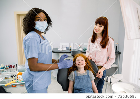 Young smiling mother with her cute preteen daughter, visit their pediatric dentist, African woman, for regular teeth checkup at stomatology clinic. Child with mom at dentist's office Young smiling mother with her cute preteen daughter, visit their pediatric dentist, African woman, for regular teeth checkup at stomatology clinic. Child with mom at dentist's office 72536685