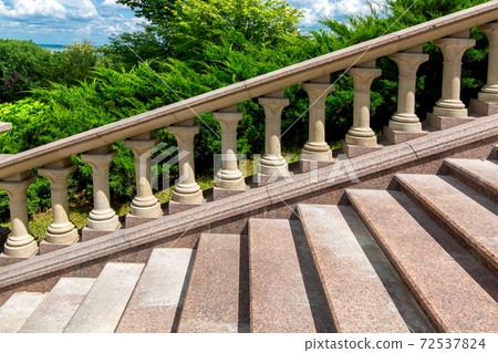 granite stone stairs details of steps and railings with balustrades in the background landscape with thuja bushes and cloudy sky on a sunny summer day. granite stone stairs details of steps and railings with balustrades in the background landscape with thuja bushes and cloudy sky on a sunny summer day. 72537824