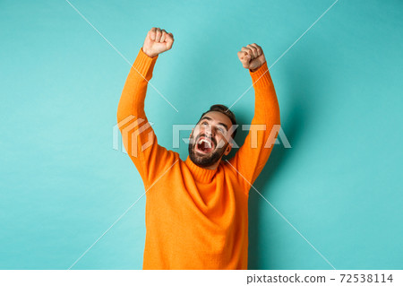 Happy man triumphing and feeling rejoice of winning, celebrating victory, standing over light blue background Happy man triumphing and feeling rejoice of winning, celebrating victory, standing over light blue background 72538114