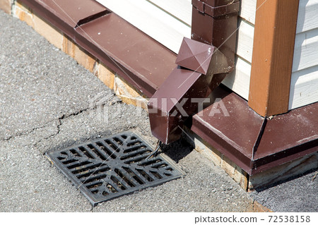 stormwater pipe on the wall of the building facade with rainwater drainage into the drainage system with a sewer manhole grill. 72538158