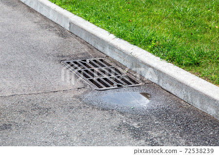 manhole grille of the drainage system on the asphalt road with a puddle after the rain. manhole grille of the drainage system on the asphalt road with a puddle after the rain. 72538239