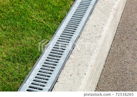 iron drainage system, closeup of an iron grille along a asphalt road and green grass. 72538265