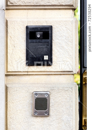 An intercom with a call button and a camera with a microphone on a stone wall with a rusticate on the bottom of the card reader for access. 72538294