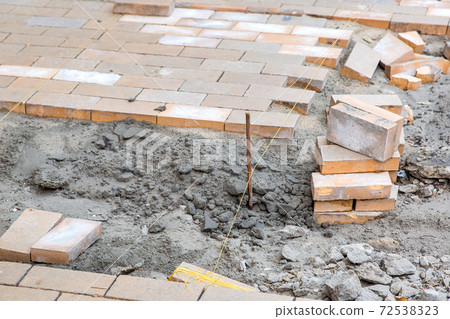 paving of a new sidewalk from rectangular stone tiles according to the marks of the stretched thread of the level, a close-up of the repair work of the stone path. 72538323