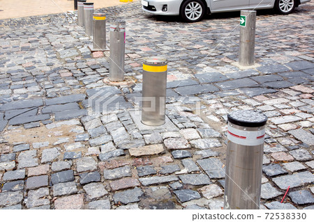 the car is waiting near electric gray hydraulic bollard with a yellow reflective stripe barrier regulating traffic in the old city center with paving stones, closeup details. 72538330