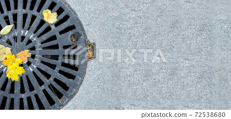 manhole cover round black metal lattice of improvement city pedestrian sidewalk paved with granite gray tiles close-up view autumn season with fallen yellow leaves with copy space, nobody. 72538680