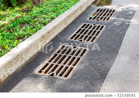hatch storm system with a rusty grate in the asphalt road surface with a stone curb. hatch storm system with a rusty grate in the asphalt road surface with a stone curb. 72539591