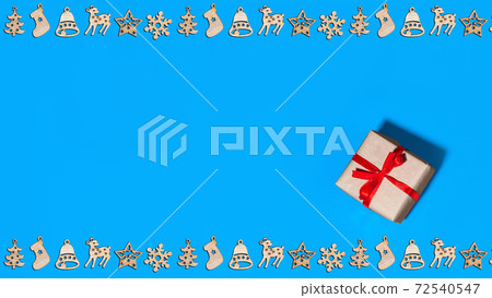 Christmas greeting card with wooden figurines on theme of new year celebration and gift box packed in craft paper with bow of red ribbon isolated on blue background, top view copy space. Christmas greeting card with wooden figurines on theme of new year celebration and gift box packed in craft paper with bow of red ribbon isolated on blue background, top view copy space. 72540547