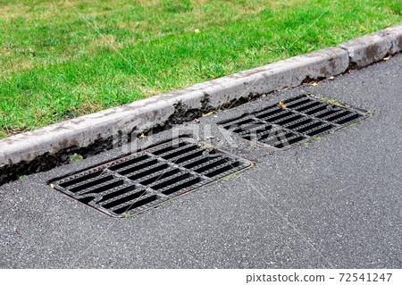 drainage system of an asphalt road with a black manhole grill for sewage near the border on sunny summer day. 72541247