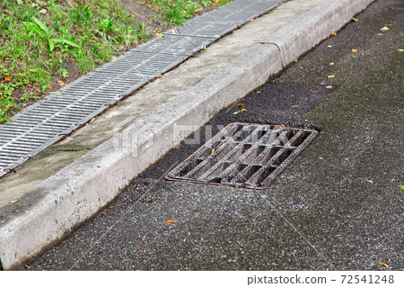 storm systems on an asphalt road a manhole grille behind a curb a drainage system grid after rain. storm systems on an asphalt road a manhole grille behind a curb a drainage system grid after rain. 72541248