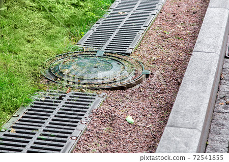 round manhole cover of drainage system on the side of the road with an iron grate and pebbles. round manhole cover of drainage system on the side of the road with an iron grate and pebbles. 72541855